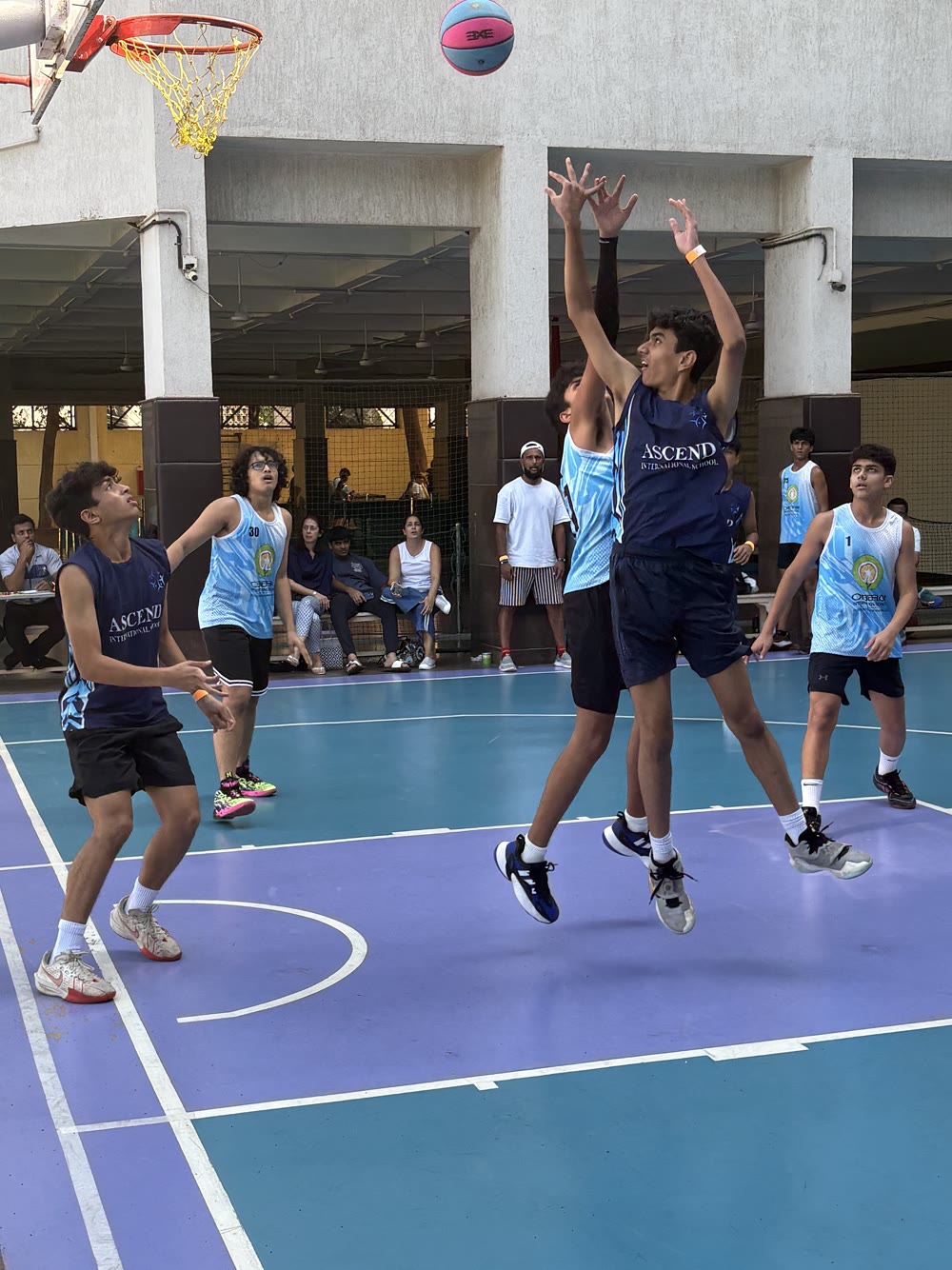 Arjun in a navy Ascend jersey jumps for a rebound beneath the hoop during an outdoor game.