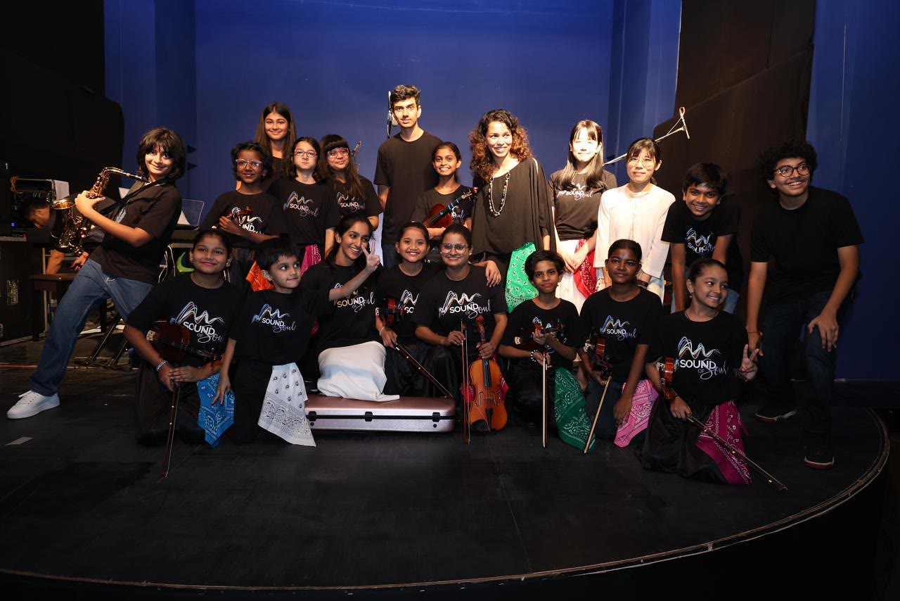 The school band and choir, in matching black T-shirts, pose together on a stage.