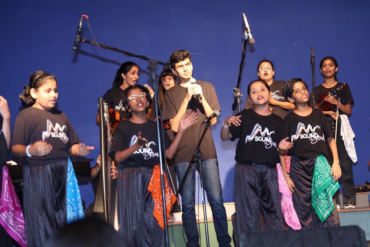 Arjun sings into a microphone on stage, with the band members around him.
